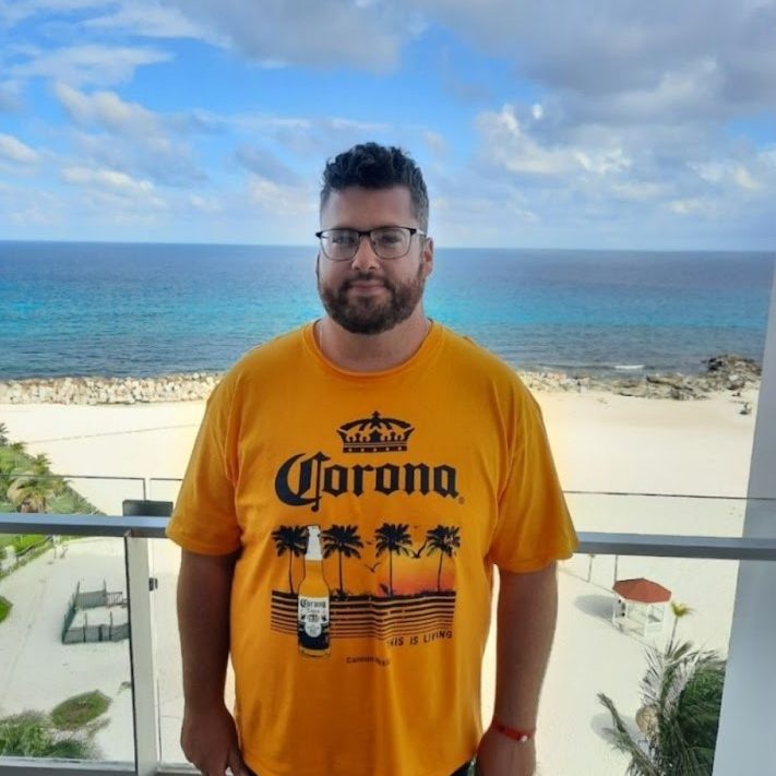 A picture of Anthony Justus standing on a balcony overlooking the beach in a tropical vacation resort setting.